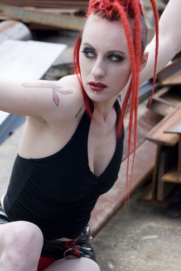 17P Chica punk de pelo rojo posa desnuda con botas de plataforma en un recinto industrial
