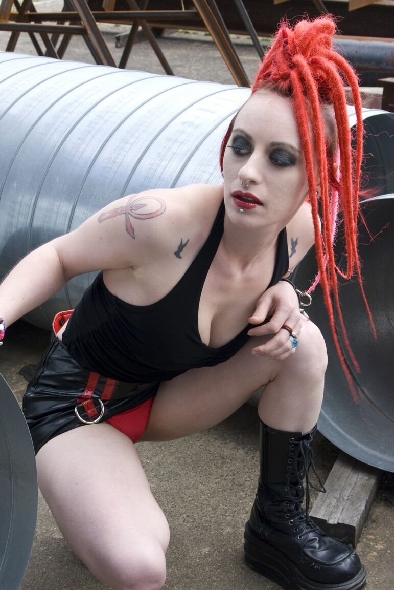 17P Chica punk de pelo rojo posa desnuda con botas de plataforma en un recinto industrial