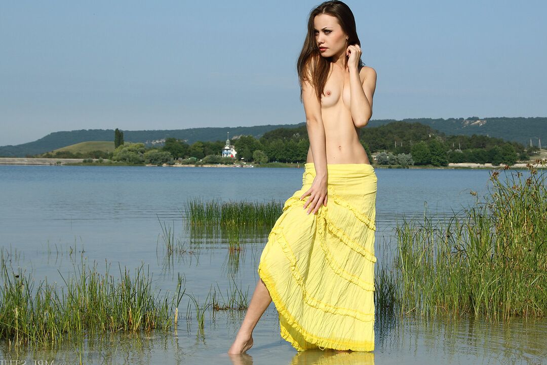12P Une belle adolescente enlève sa robe jaune avant de se tenir nue dans une eau peu profonde