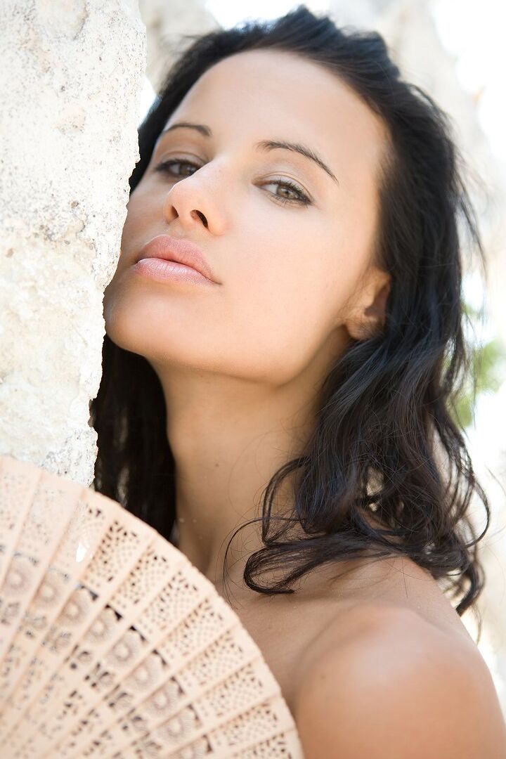 16P La modelo morena Paris posa desnuda cerca del muro de un jardín bañado por el sol