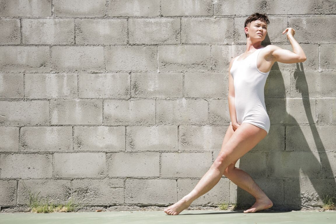 15P Short haired dyke Jiz Lee strips for nude poses against a cinder block wall