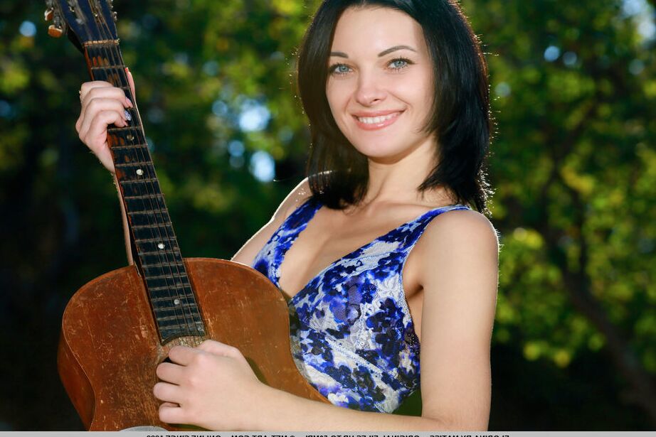 Die 18-jährige brünette Teenagerin Florina hält eine Akustikgitarre in der Hand, während sie sich im Freien auszieht