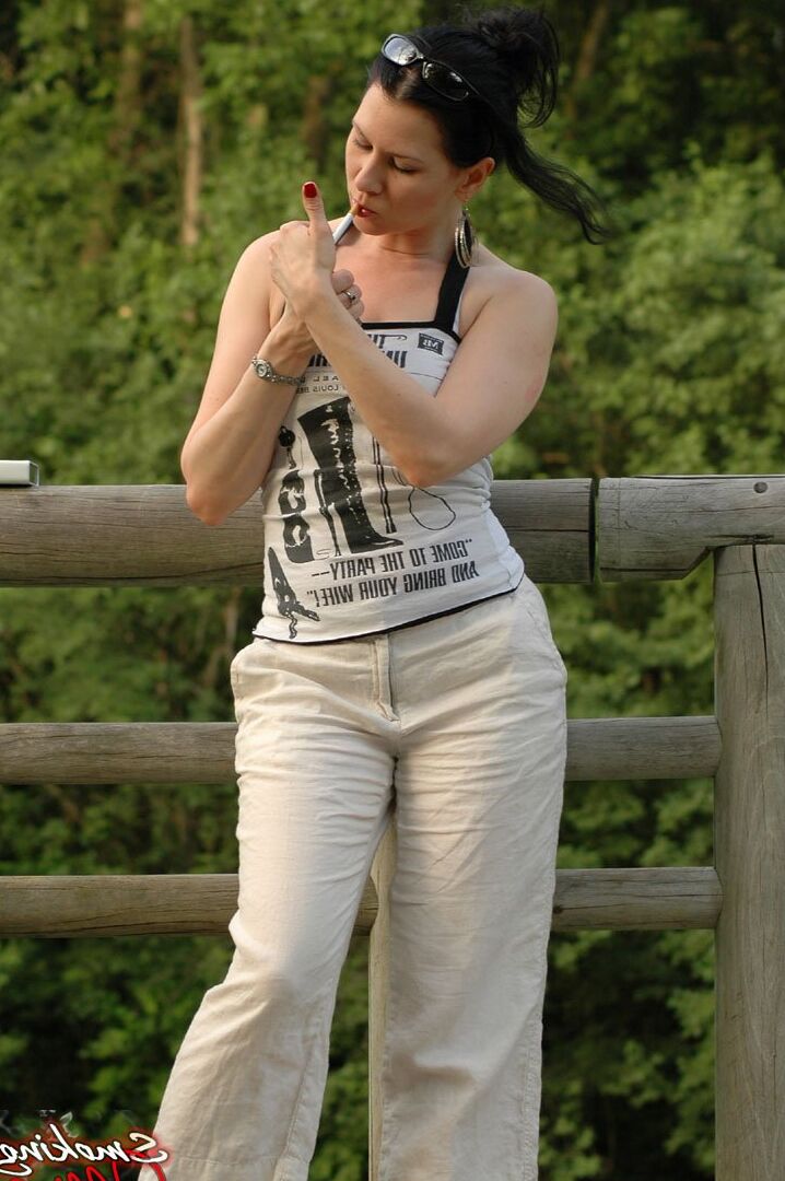 15P Solo girl smokes a cigarette up against a rail fence while fully clothed