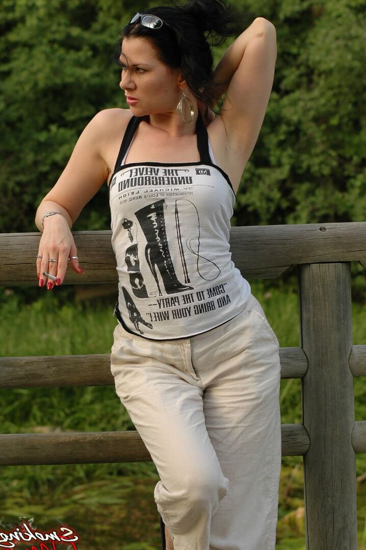 15P Solo girl smokes a cigarette up against a rail fence while fully clothed