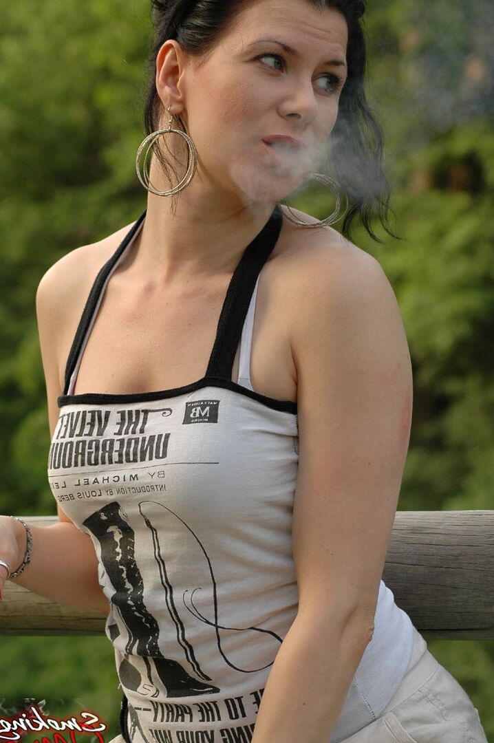 15P Solo girl smokes a cigarette up against a rail fence while fully clothed