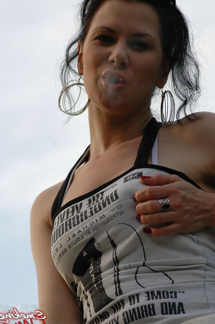 15P Solo girl smokes a cigarette up against a rail fence while fully clothed