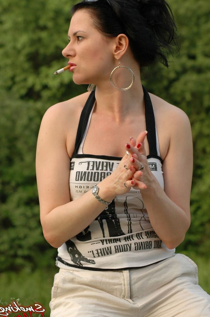 15P Solo girl smokes a cigarette up against a rail fence while fully clothed