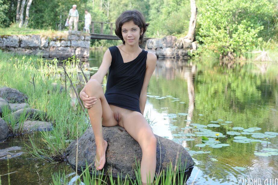 20P Young brunette shows her tight slit in the nude on rock by a pond