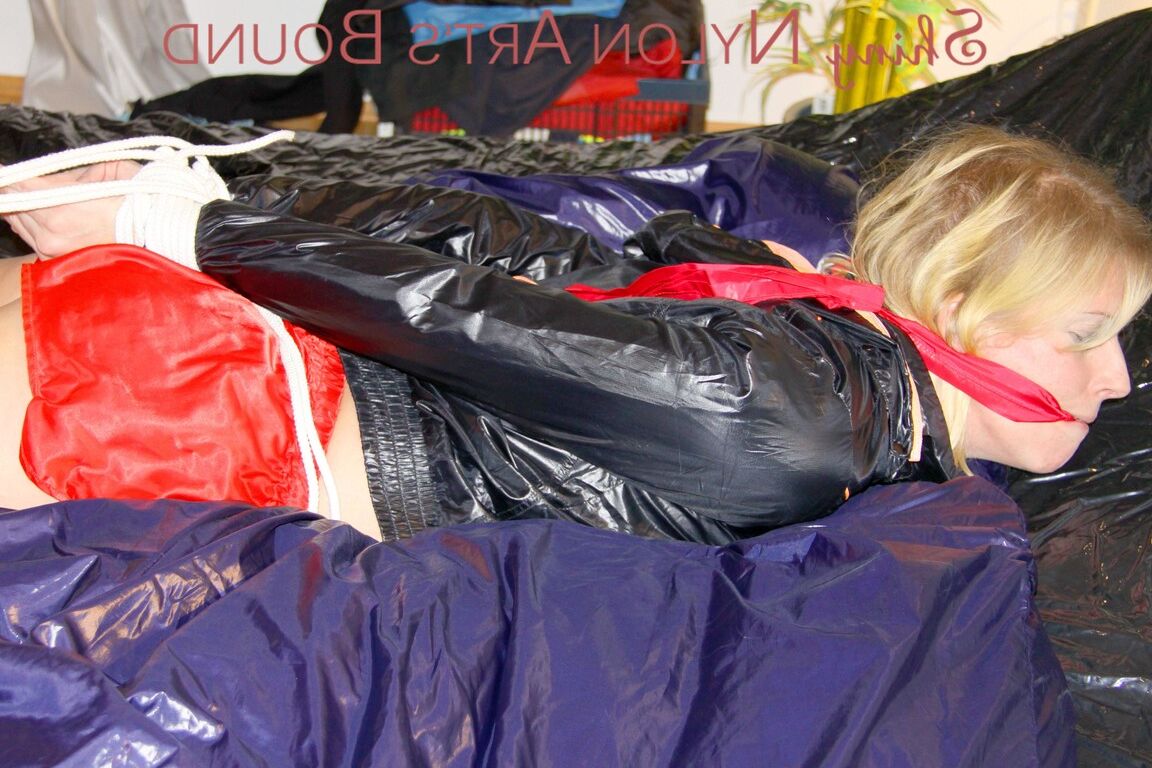 16P Пиа связана и с кляпом во рту лежит на кровати в суперсексуальных блестящих красных нейлоновых шортах и