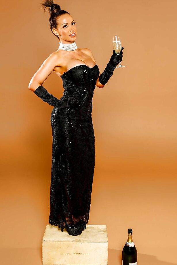 16P Die heiße MILF Nikki Benz posiert in ihrem schwarzen Kleid mit einem Weinglas