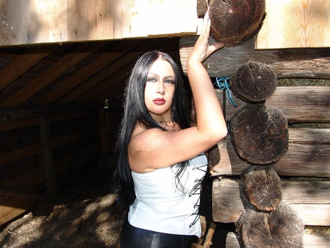 16P Lady Angelina gótica de pelo oscuro muestra sus grandes tetas y su coño junto a un edificio de troncos