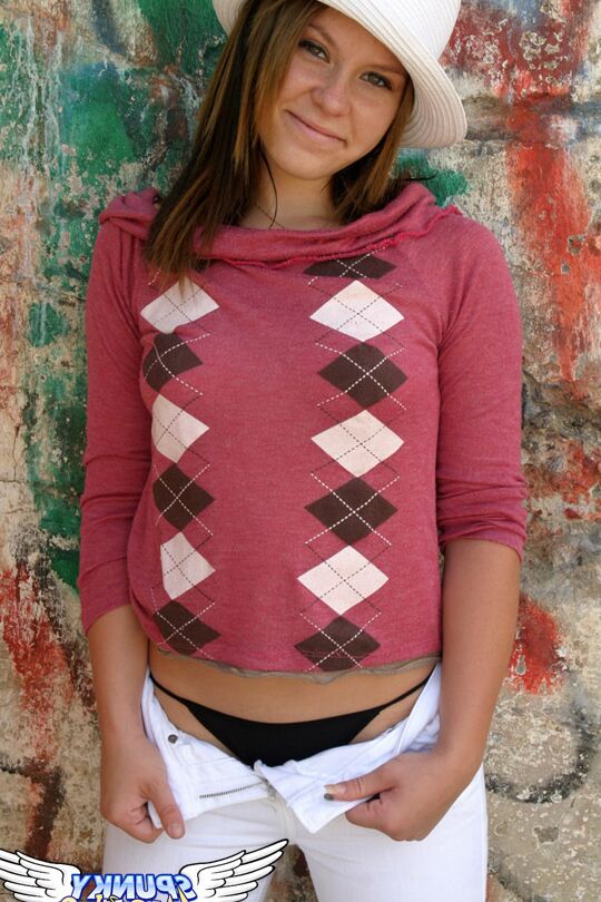 12P Redhead amateur Kandie takes off a hat and hoodie by a concrete wall