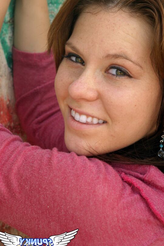 12P Redhead amateur Kandie takes off a hat and hoodie by a concrete wall
