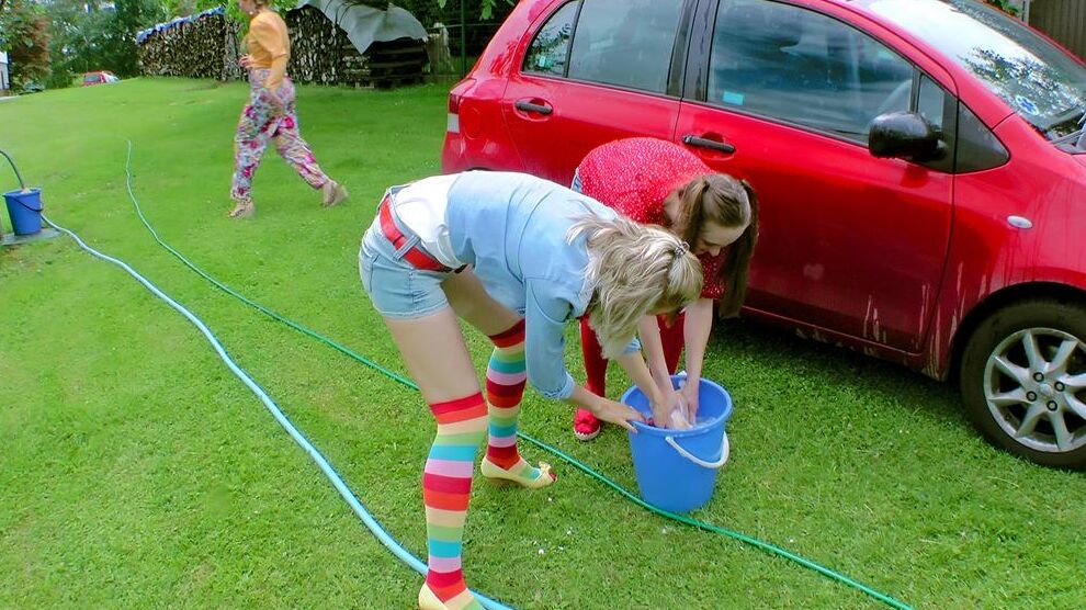 14P Young girls soak each other in a backyard while washing a compact vehicle