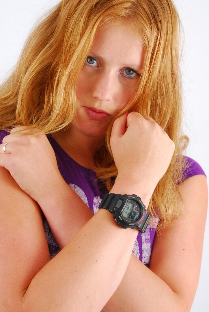 Die 16P natürliche Rothaarige Judy modelliert eine schwarze G-Shock-Uhr, während sie vollständig bekleidet ist