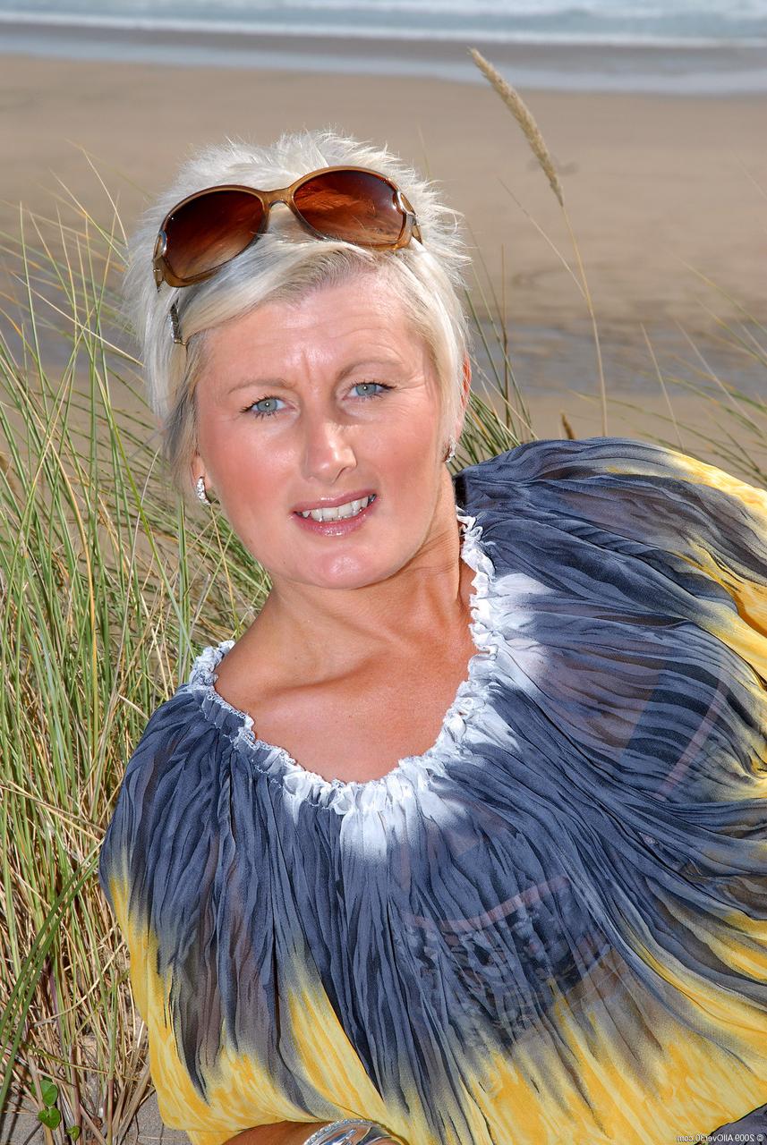 20P Sally T, blonde mature aux cheveux courts, expose ses petits tétons et sa chatte percée.