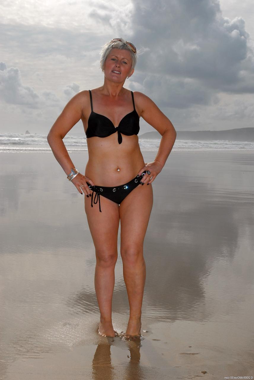 20P Sally T, blonde mature aux cheveux courts, expose ses petits tétons et sa chatte percée.