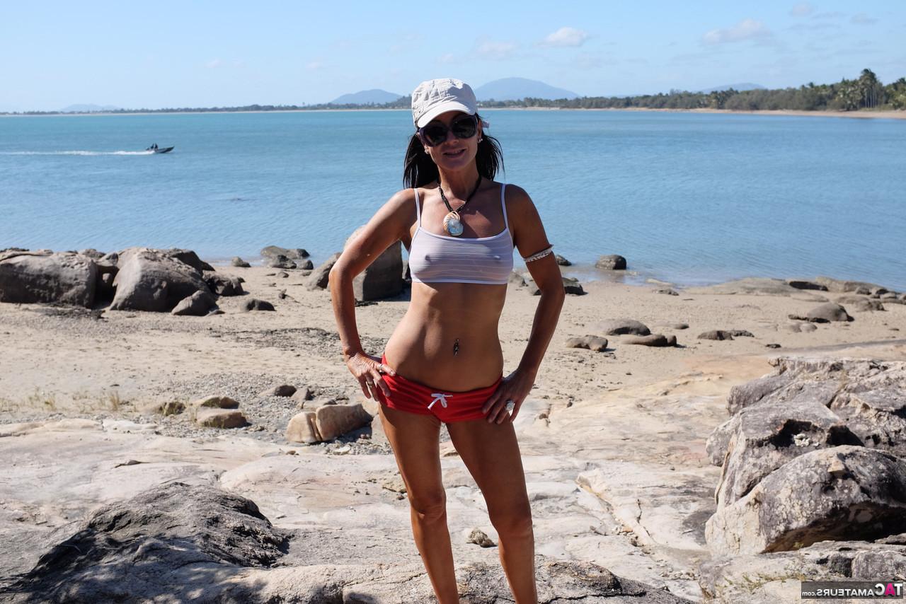 16P Die brünette MILF Roxeanne zieht sich am Strand mit Sonnenbrille aus