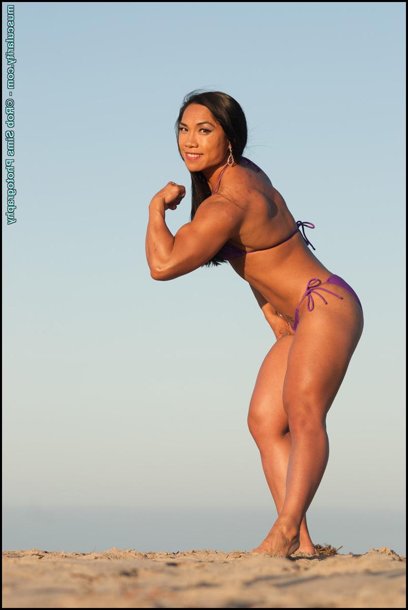 15P Asian bodybuilder Tram Nguyen flexes on a beach while wearing a purple bikini