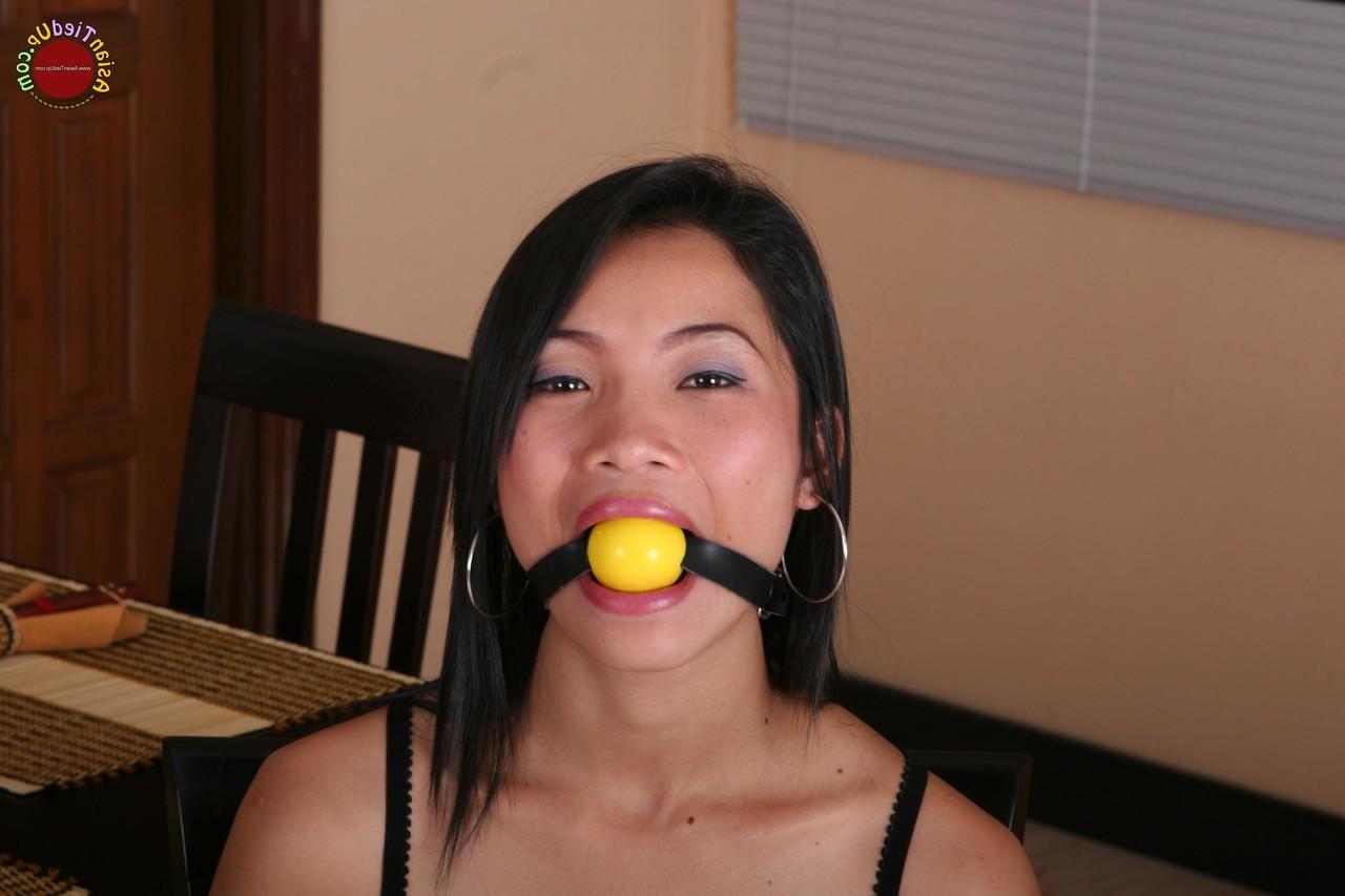 16P Une fille asiatique se bat contre un bâillon-boule alors qu'elle est attachée à une chaise de cuisine