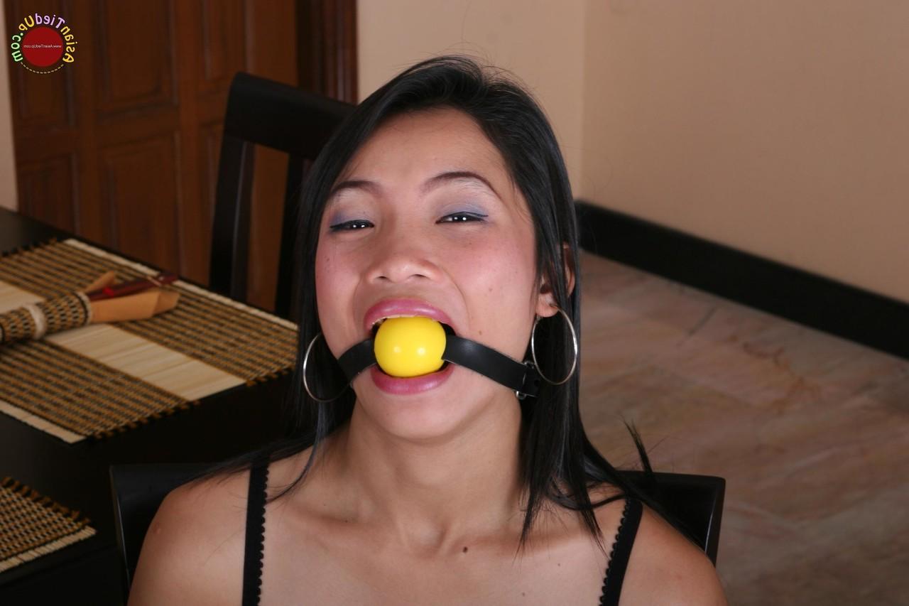 16P Une fille asiatique se bat contre un bâillon-boule alors qu'elle est attachée à une chaise de cuisine