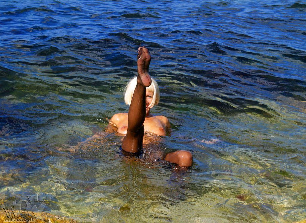 12P Rubia platino se quita las medias desnuda sobre una roca en el agua