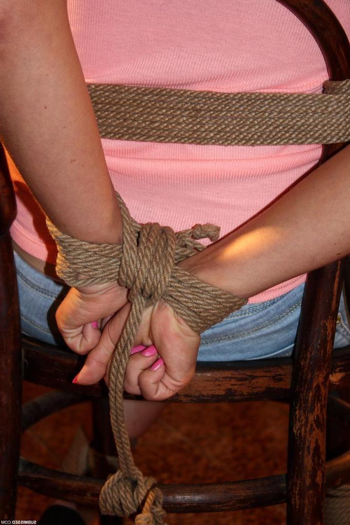 12P Blonde Frau in Jeansshorts ist geknebelt und an einen Stuhl in einem leeren Raum gefesselt