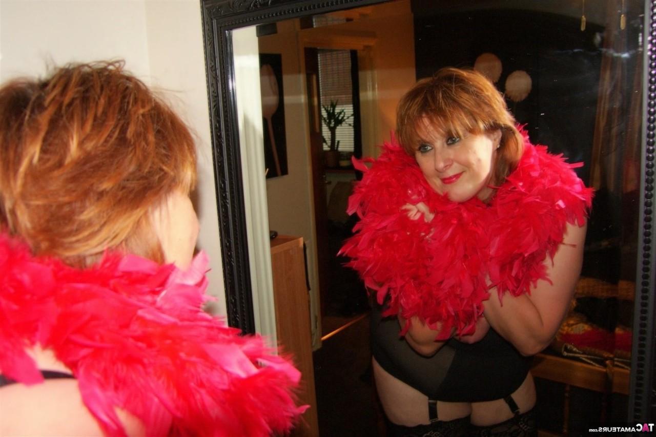16P Une rousse plus âgée montre ses seins et sa chatte drapée dans un boa en plumes.