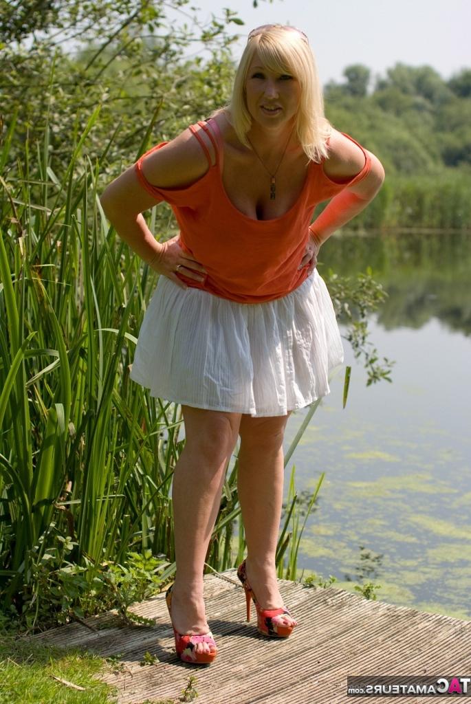20P Melody, grosse femme blonde aux gros seins, se déshabille sur un quai au bord du lac.