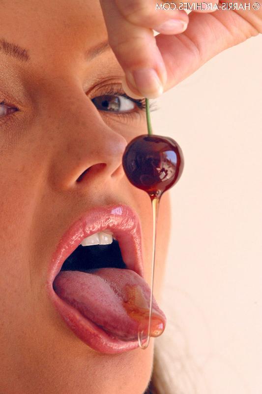 15P Das hübsche Mädchen Sandra Shine kräuselt ihre Zunge, während sie Saft aus einer Kirsche lutscht