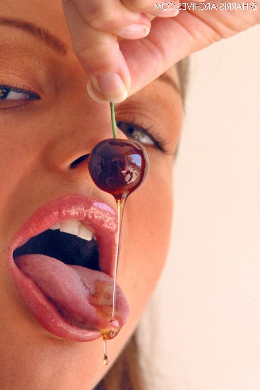 15P Das hübsche Mädchen Sandra Shine kräuselt ihre Zunge, während sie Saft aus einer Kirsche lutscht