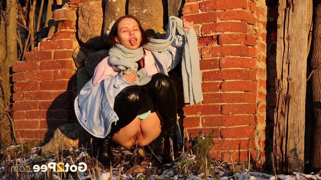 15P Pinkycat, une asiatique, s'accroupit pour pisser sur un sol gelé près d'un mur de briques.