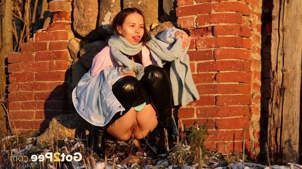 15P Pinkycat, une asiatique, s'accroupit pour pisser sur un sol gelé près d'un mur de briques.