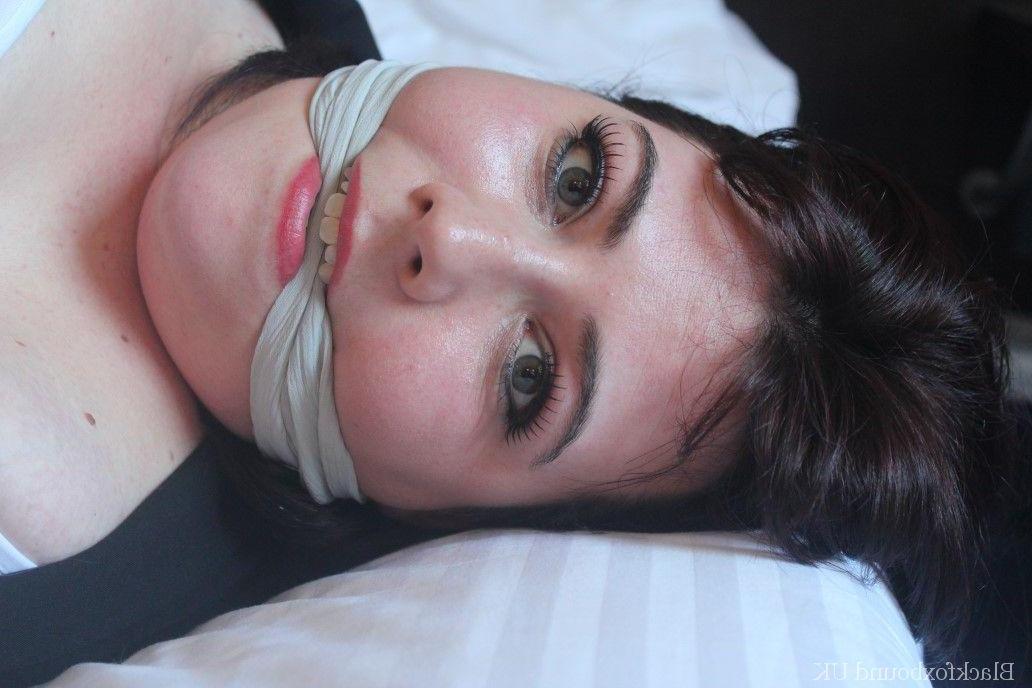 16P Mujer de cabello oscuro muestra su sostén mientras está atada y amordazada en una cama