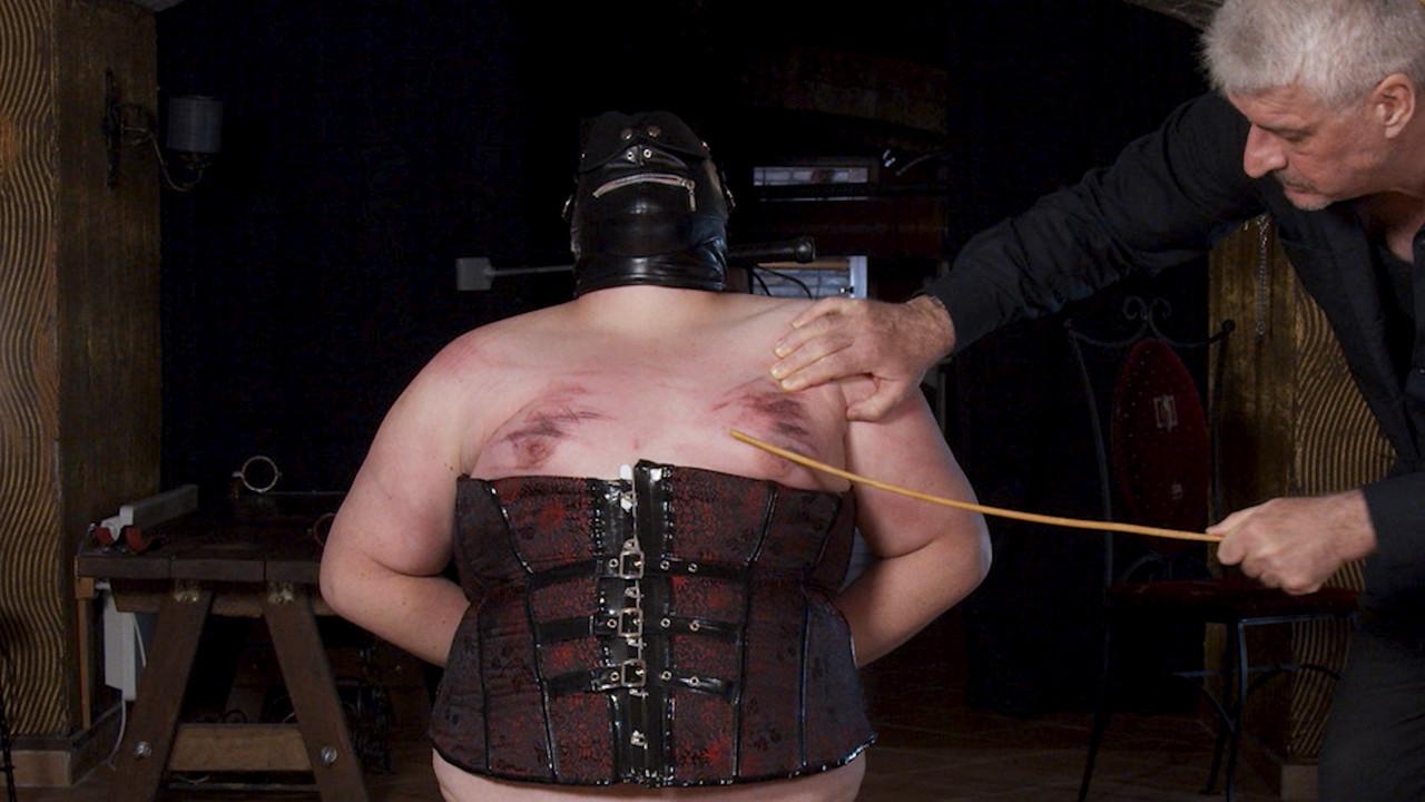 14P Une grosse femme mature portant un masque se fait canner et serrer les seins pendant qu'elle est ligotée
