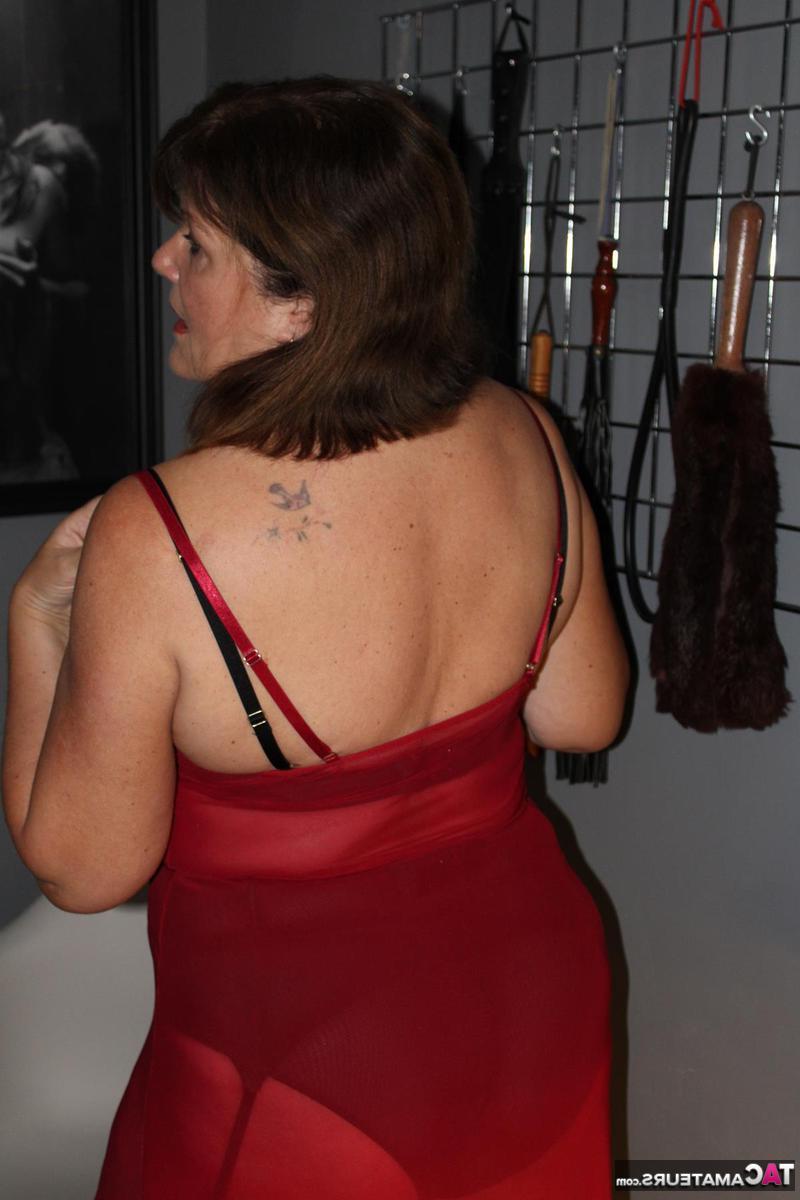 16P Cassandra UK, une femme mûre, modèle de la lingerie devant un mur de jouets sexuels.