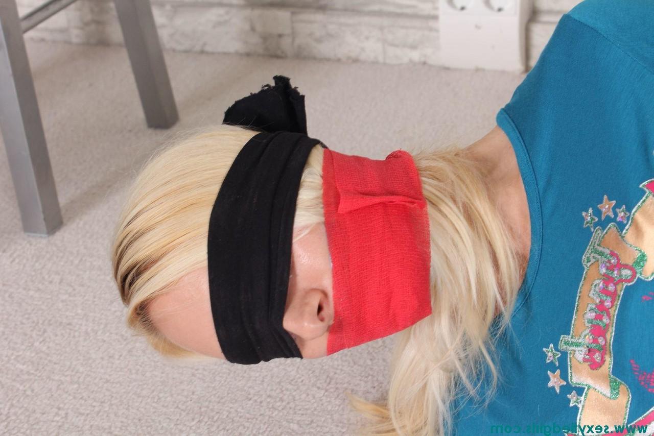16P Une fille blonde a les yeux bandés et est attachée avec ses vêtements.