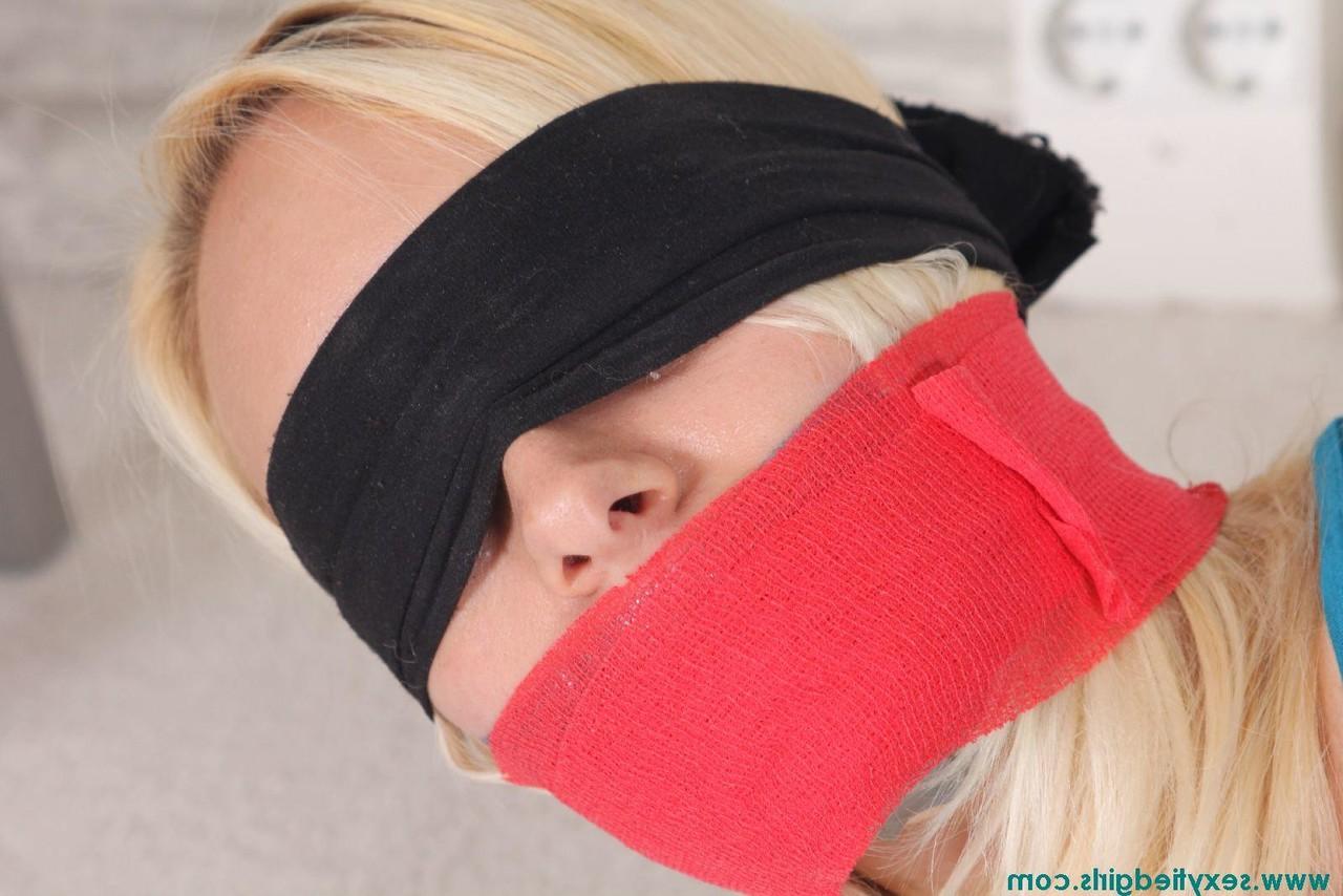 16P Une fille blonde a les yeux bandés et est attachée avec ses vêtements.