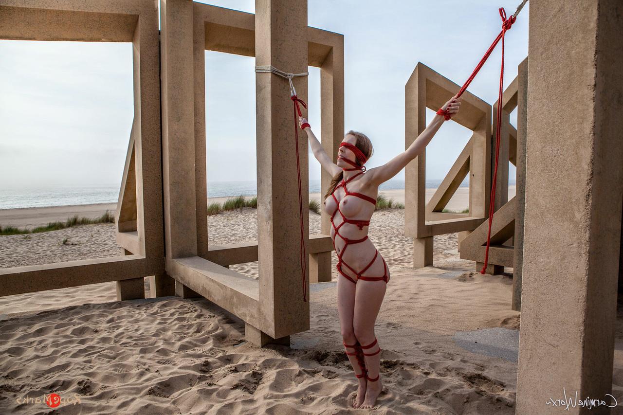 16P White girl Carmine Worx is tied with ropes to construction beams on a beach
