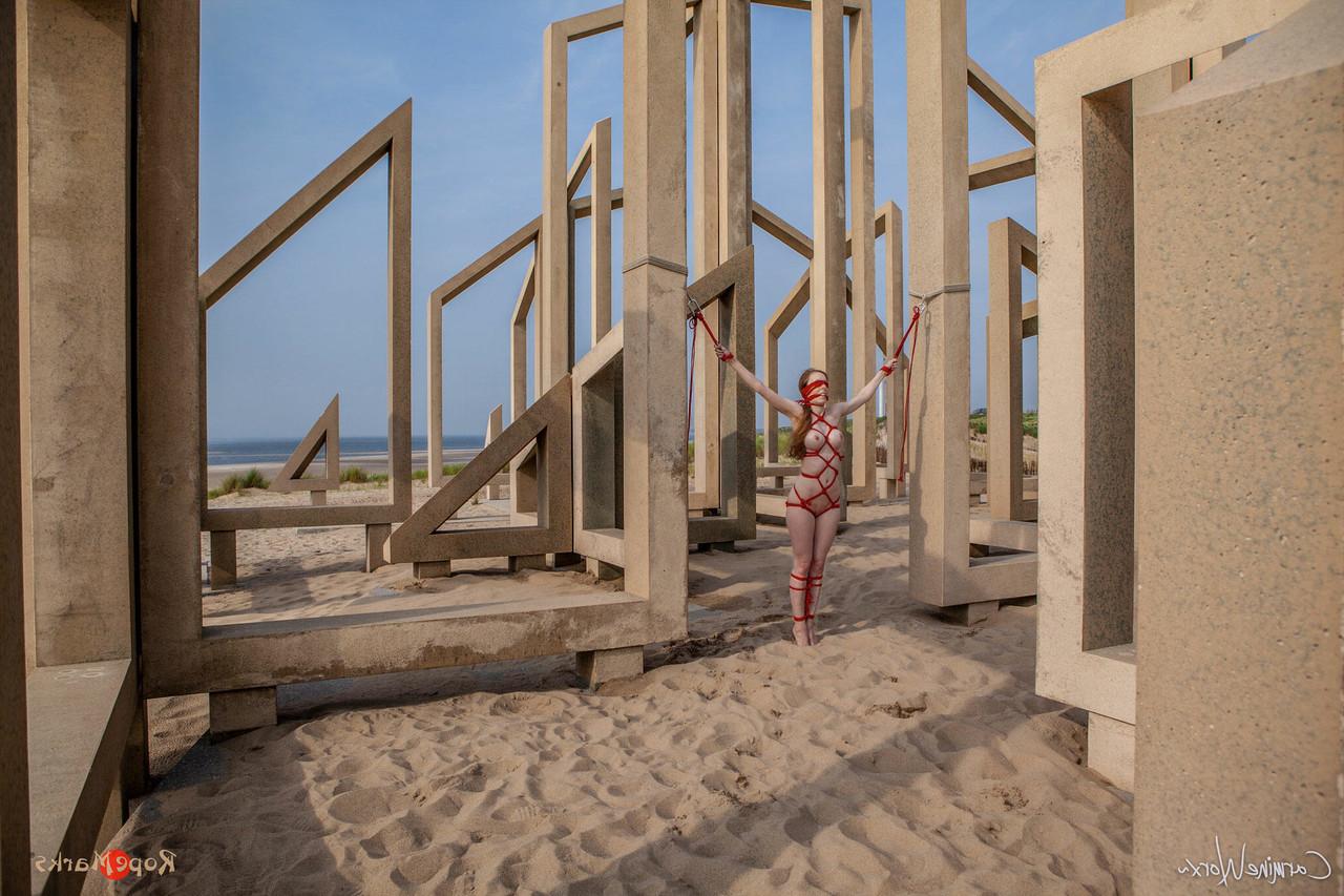 16P White girl Carmine Worx is tied with ropes to construction beams on a beach