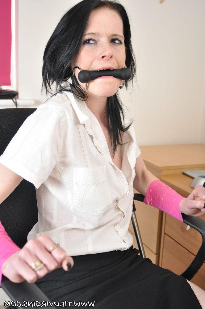 12P Une fille aux cheveux noirs arbore un mors de cheval alors qu'elle est attachée à une chaise de bureau en tenue de bureau