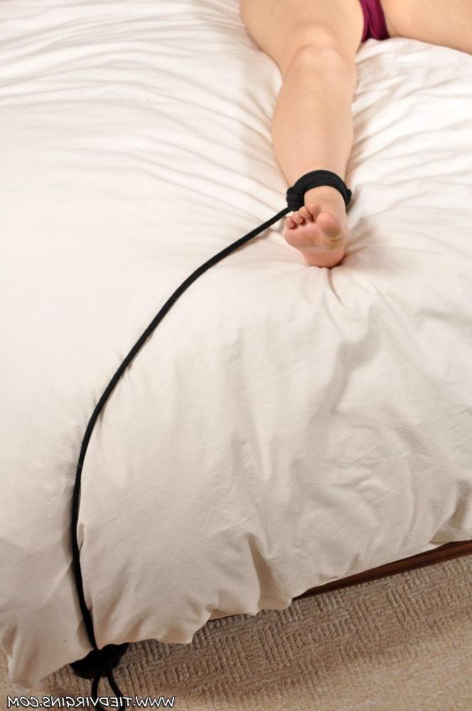 12P Oben-ohne-Blondine ist an Handgelenken und Knöcheln mit Seilen an ein Doppelbett gefesselt
