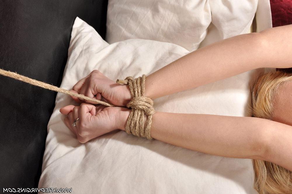 12P Oben-ohne-Blondine ist an Handgelenken und Knöcheln mit Seilen an ein Doppelbett gefesselt