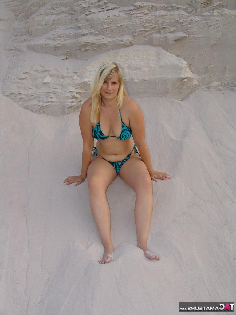 20P La blonde mature Sweet Susi enlève son bikini pour poser nue dans un bac à sable.