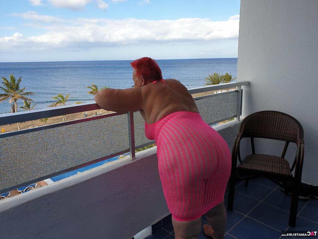 20P Fette Oma mit kurzen roten Haaren spreizt mit dem Finger ihre Muschi auf dem Balkon am Meer