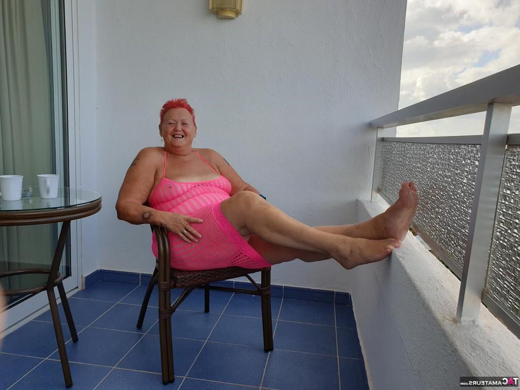 20P Fette Oma mit kurzen roten Haaren spreizt mit dem Finger ihre Muschi auf dem Balkon am Meer