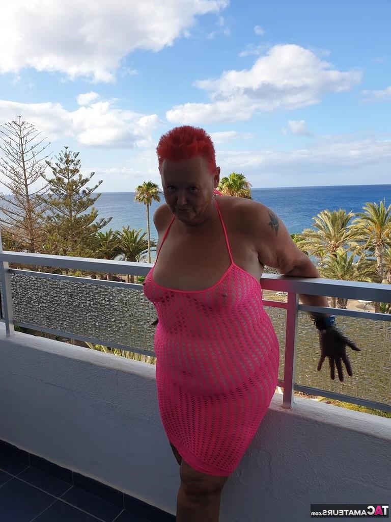 20P Fette Oma mit kurzen roten Haaren spreizt mit dem Finger ihre Muschi auf dem Balkon am Meer
