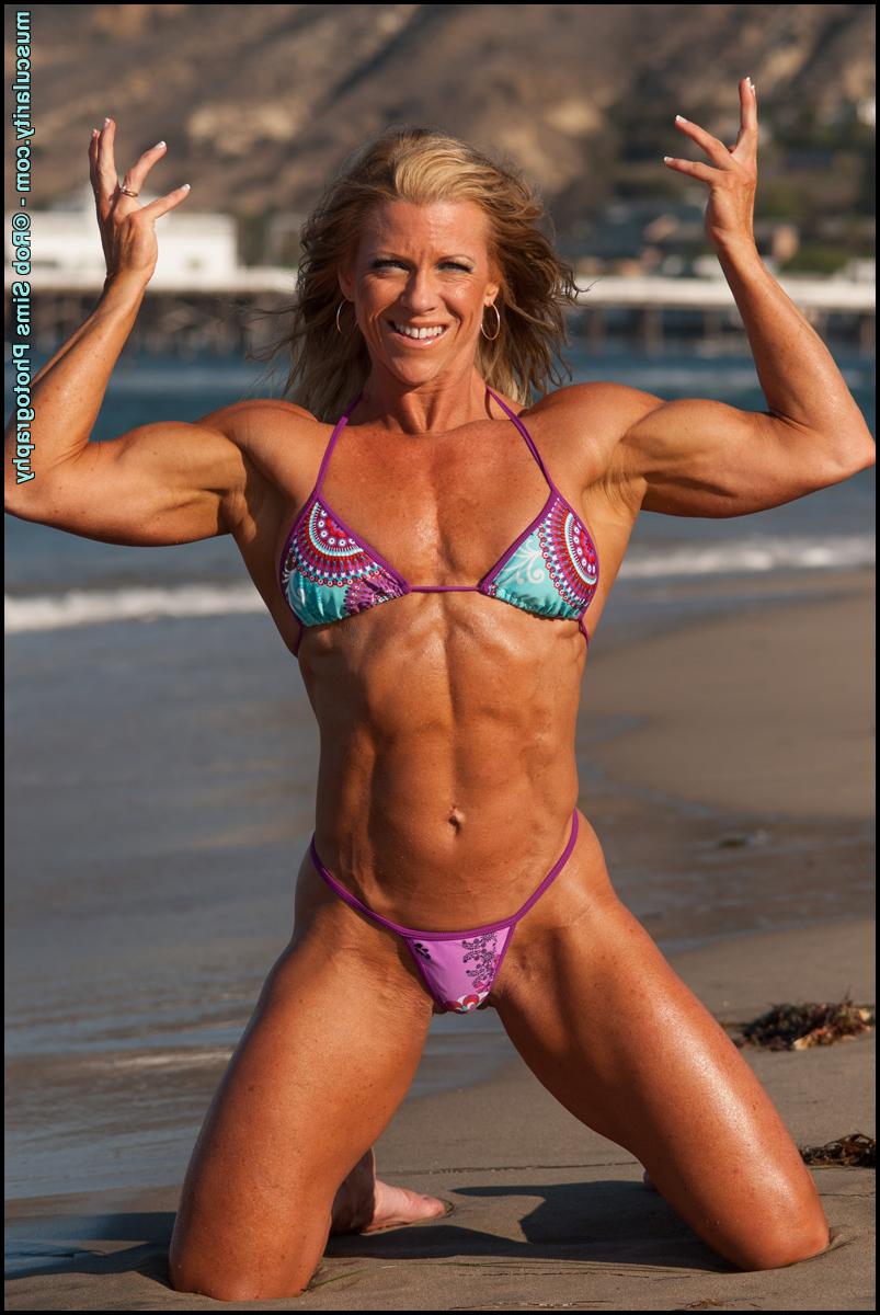 15P La bodybuildeuse blonde Amy Bowen pose sur une plage en bikini alors que les vagues arrivent.
