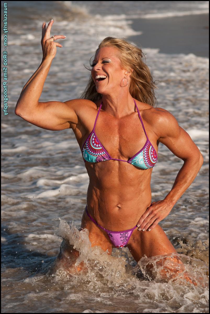 15P La bodybuildeuse blonde Amy Bowen pose sur une plage en bikini alors que les vagues arrivent.