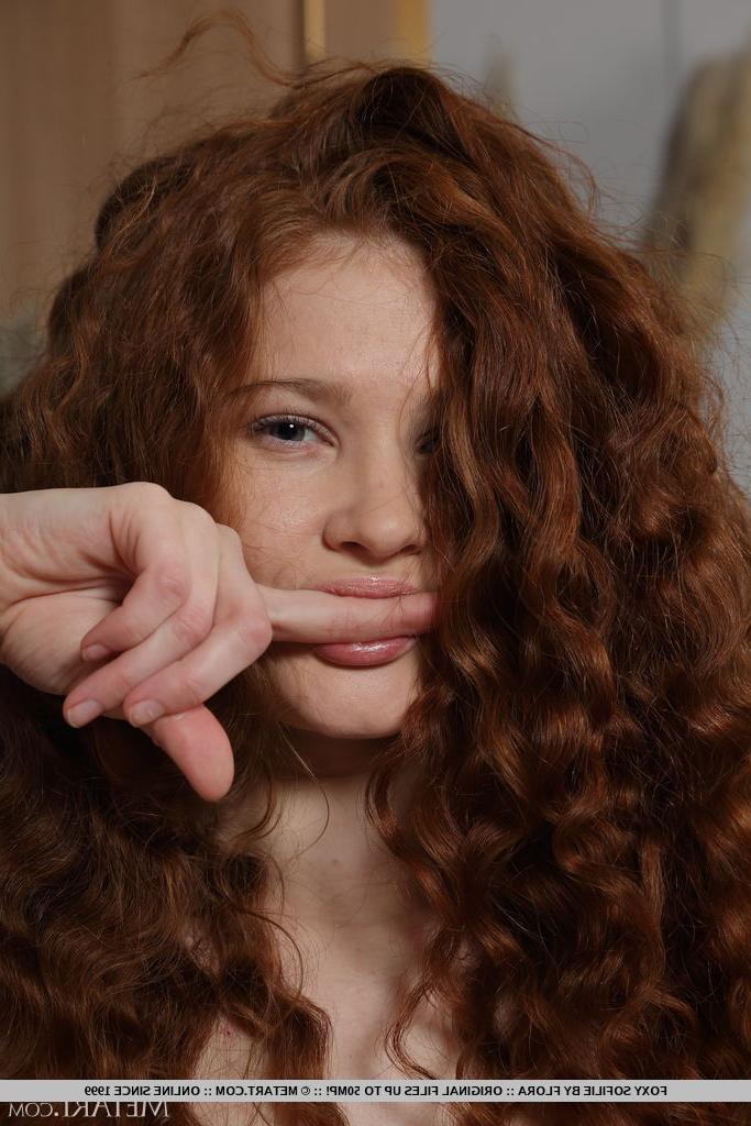 18P Foxy Sofilie, jeune fille aux cheveux roux ondulés, se met nue sur un canapé-lit.